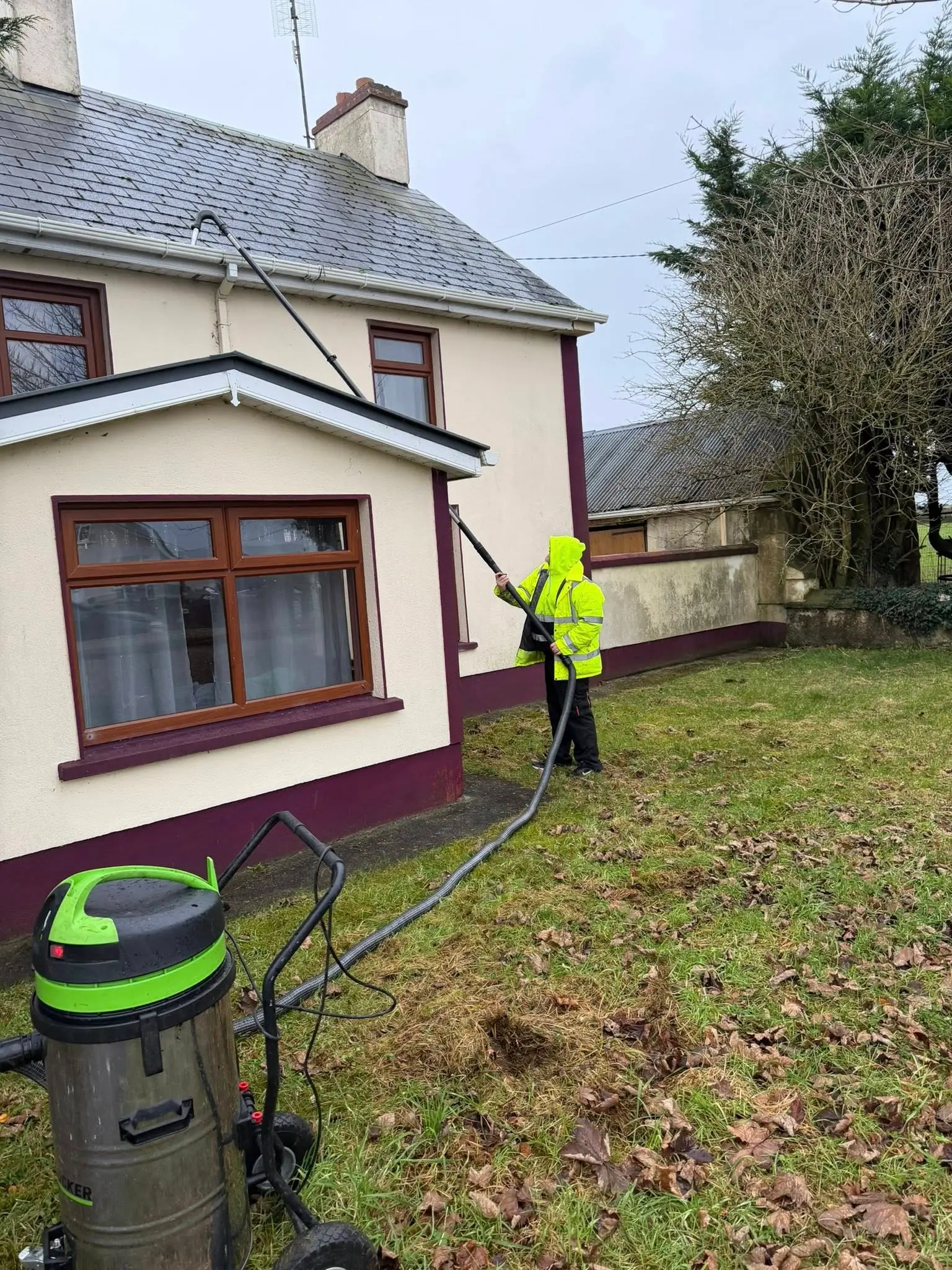 Gutter cleaning using a long vacuum pole on a country farmhouse