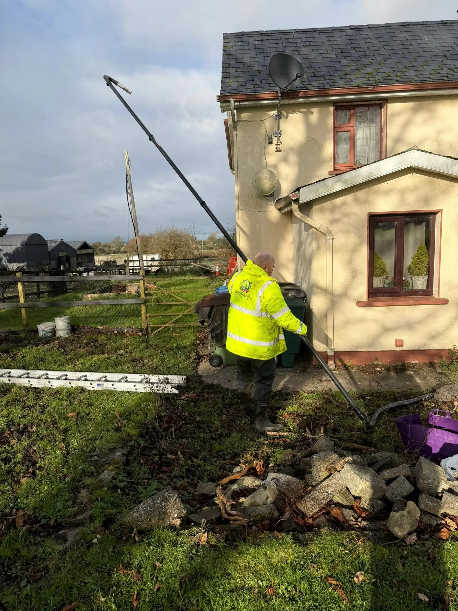 Gutter clearing with a long reach pole on a yellow country cottage in Galway